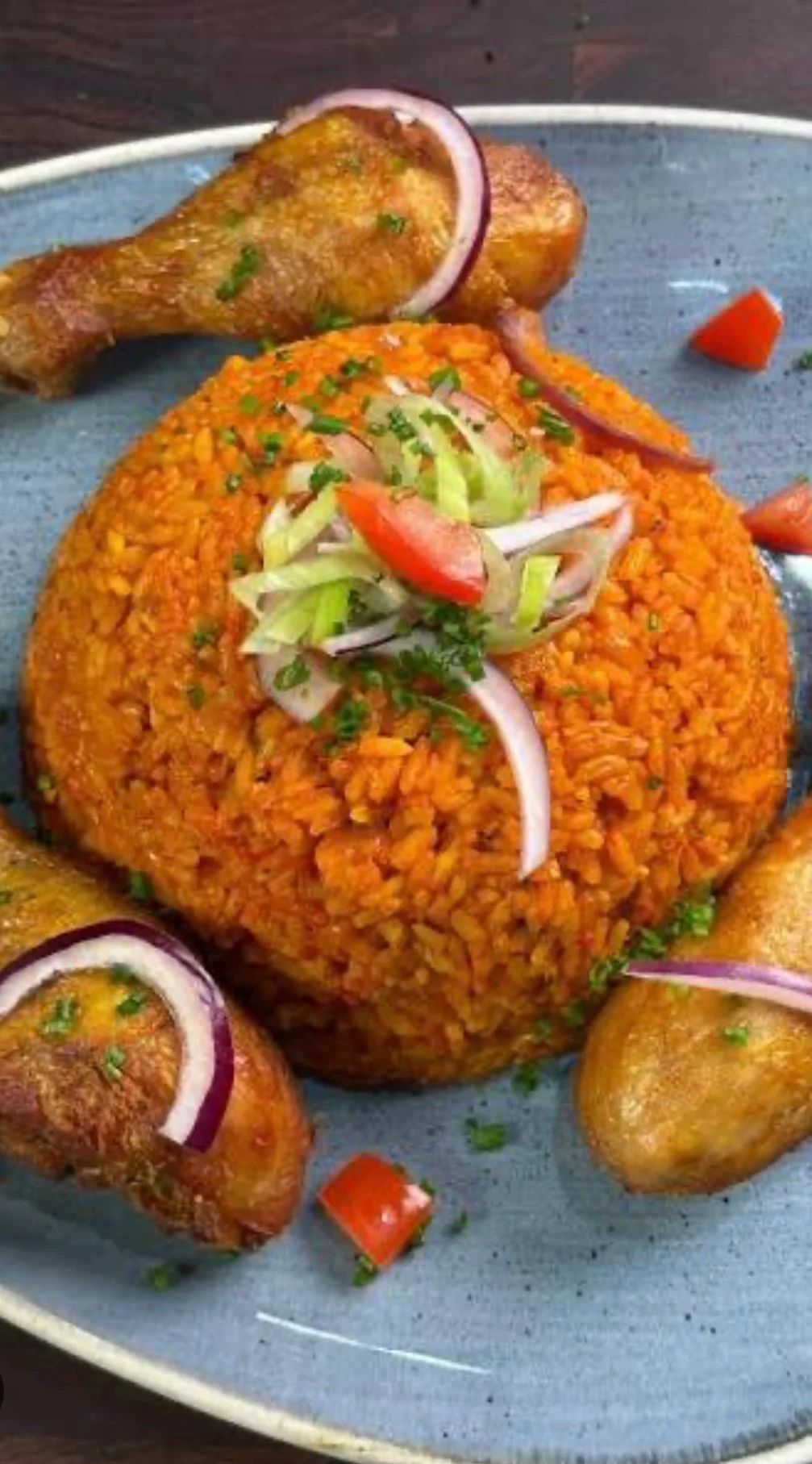 A plate of vibrant orange rice topped with diced vegetables and served with fried chicken drumsticks.