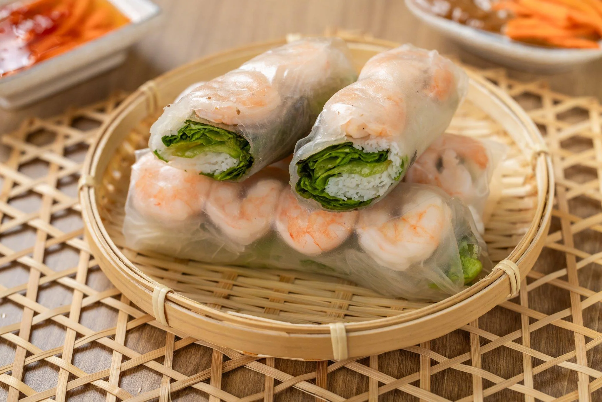 A bamboo basket containing fresh shrimp spring rolls filled with lettuce and rice, served with a dipping sauce.