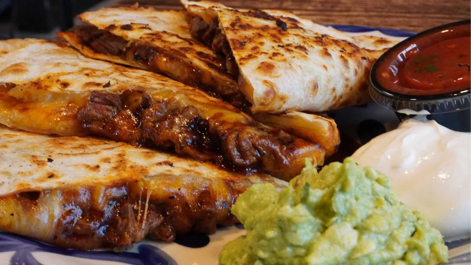 carne asada quesadilla grilled with cheese and garnished with guacomole and sour cream 
