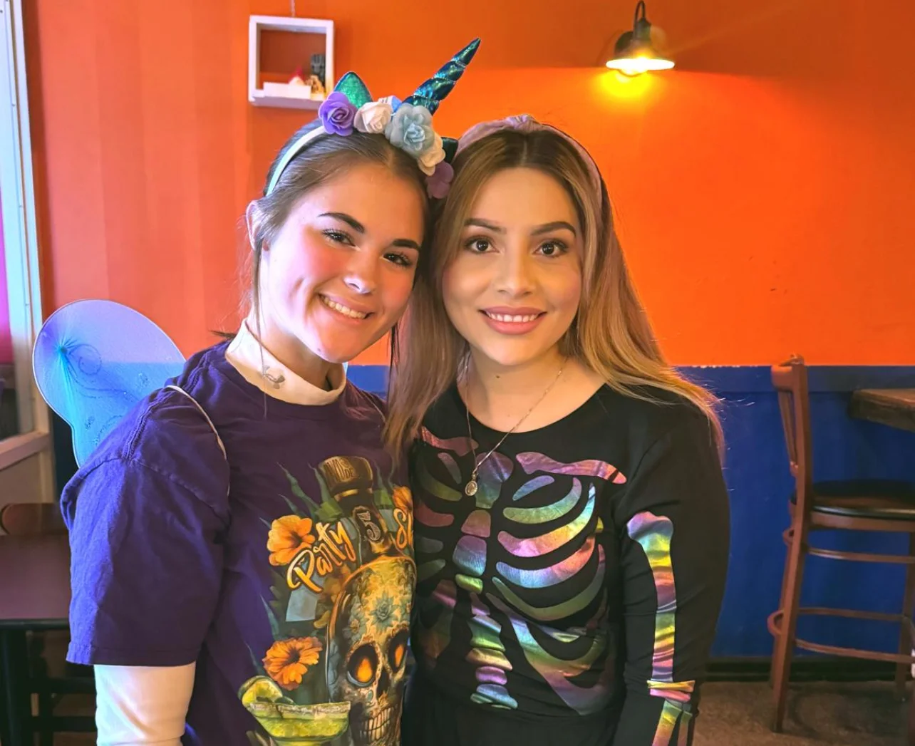 Two women in festive costumes smiling in a colorful restaurant interior