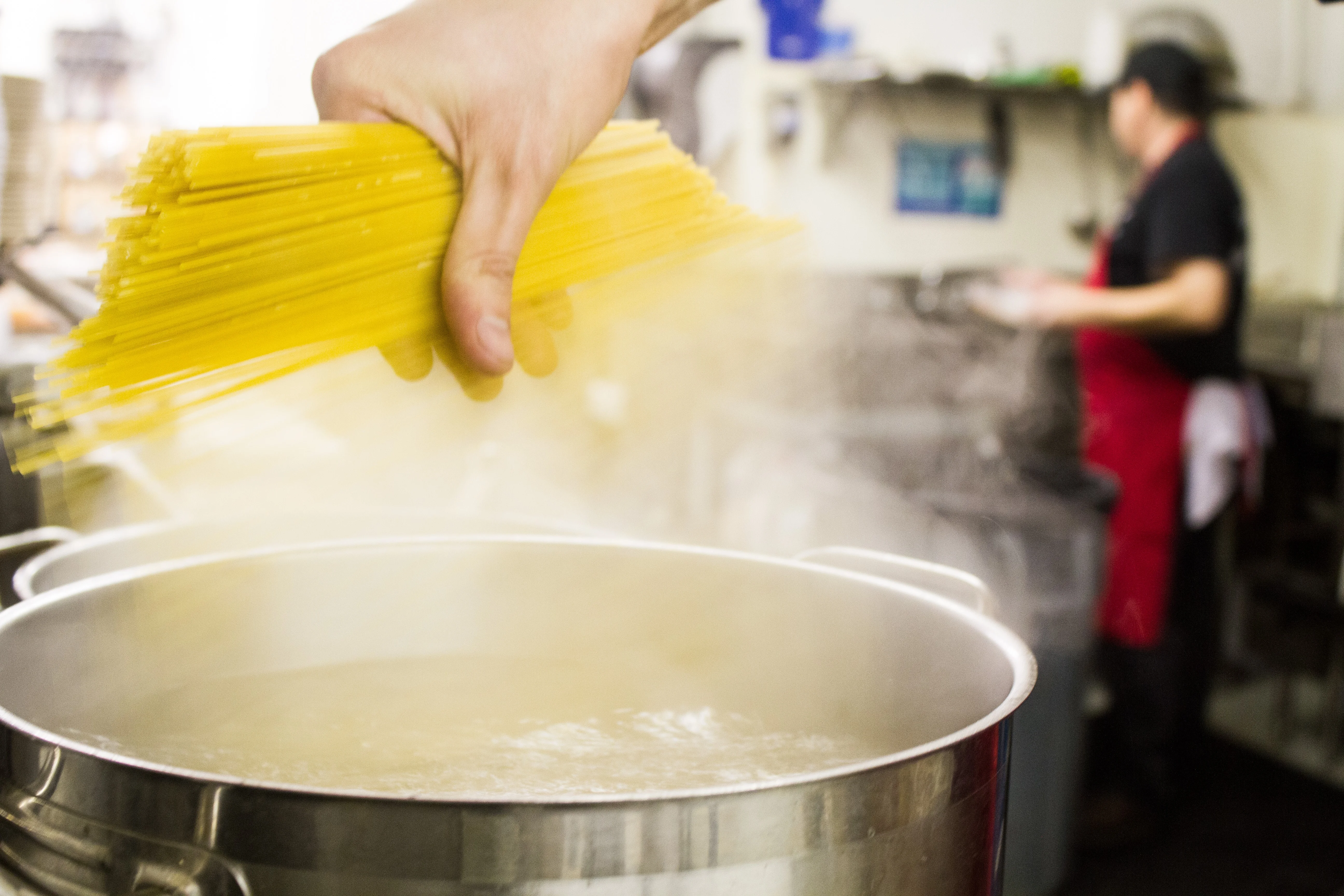 Chef adding spaghetti to boiling water in a restaurant kitchen