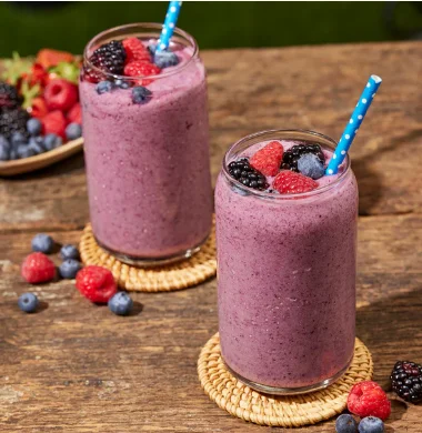 Two berry smoothies topped with fresh berries on a wooden table.