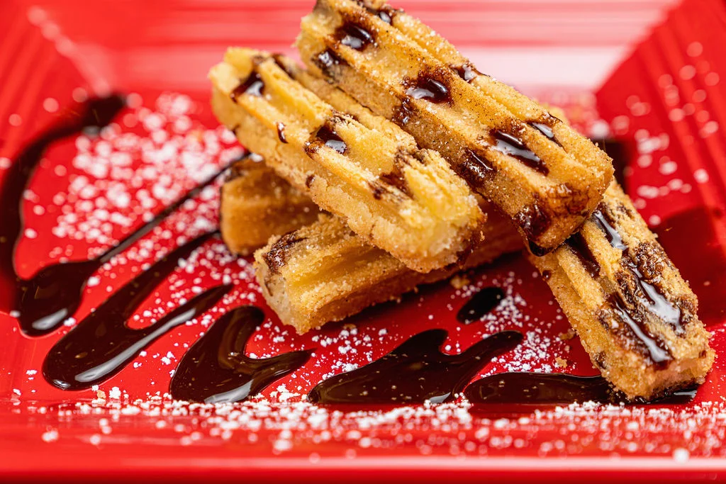 Churros drizzled with chocolate sauce on a red plate