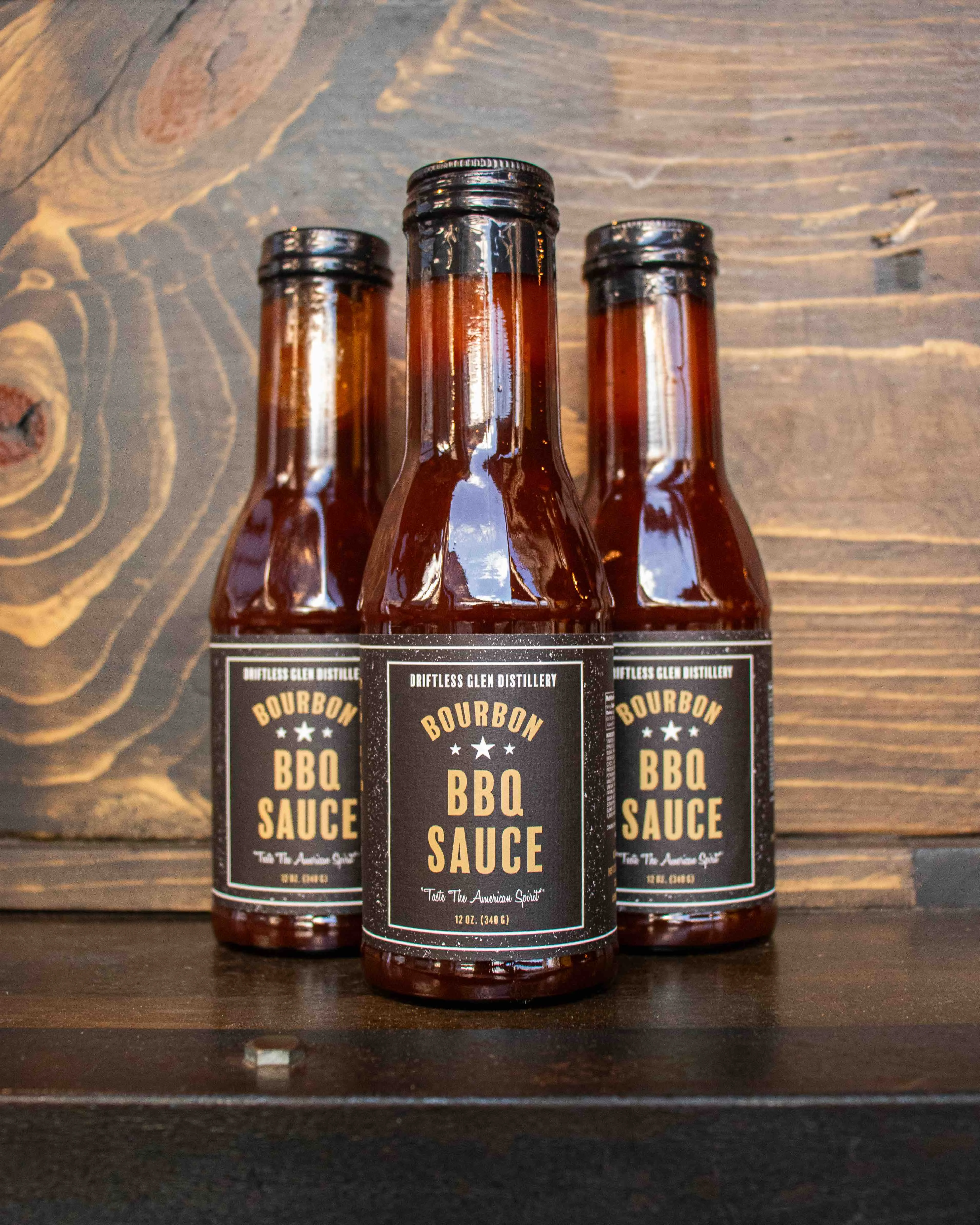 Three bottles of Bourbon BBQ Sauce sit on a wooden shelf