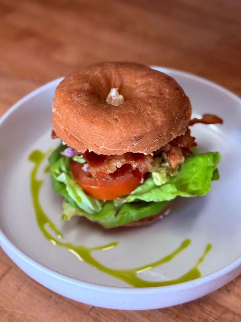 A donut sandwich with bacon, lettuce, and tomato on a plate.
