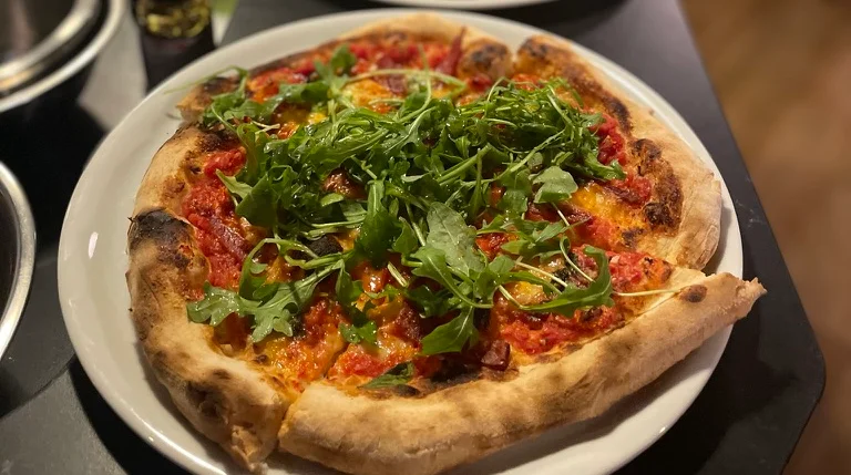 Freshly baked pizza topped with arugula in a cozy restaurant setting