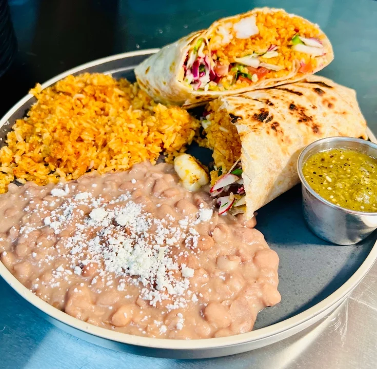 A taco topped with fish, salsa, and garnishes, accompanied by a bowl of sauce on a black plate.