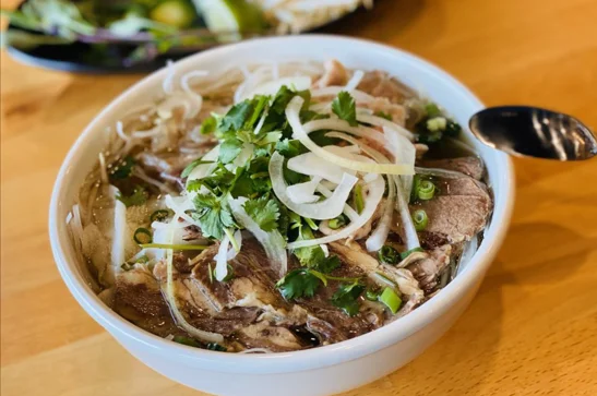 A bowl of pho with fresh herbs and ingredients, showcasing Vietnamese cuisine.