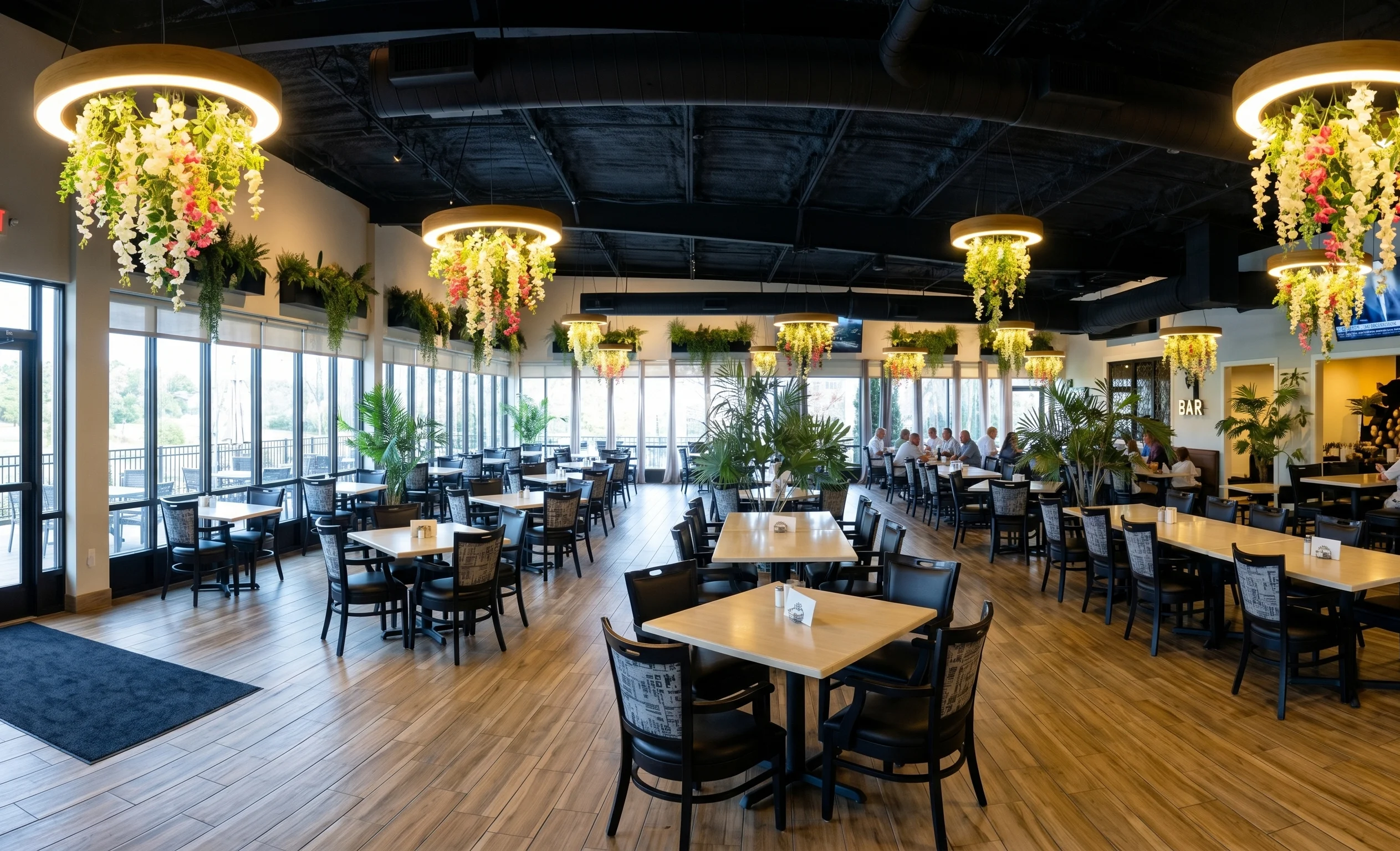 An elegantly arranged dining area with a long table set for a large group, featuring decorative hanging plants and ambient lighting.