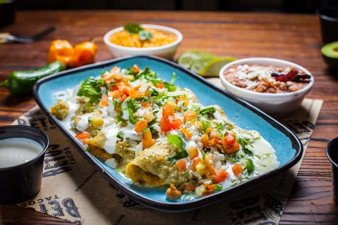 Plate of enchiladas topped with cilantro, tomatoes, and sour cream.