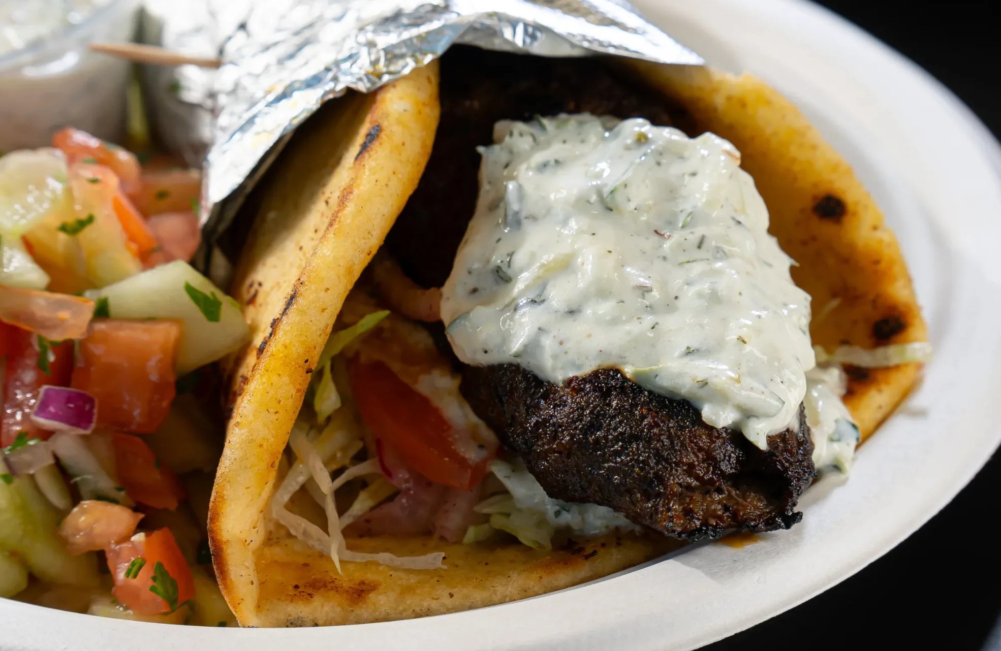 A taco filled with grilled meat, drizzled with a creamy sauce, accompanied by a side of fresh salsa made from diced tomatoes and cucumbers.