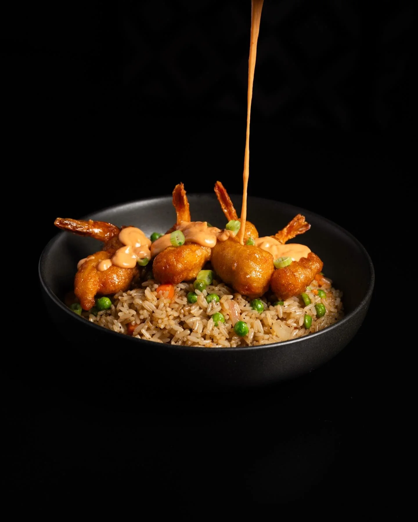Crispy shrimp with rice and spicy sauce in a black bowl