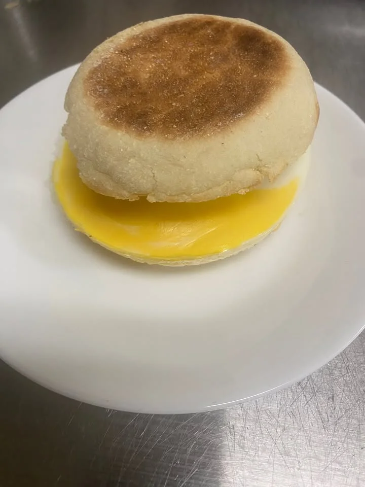 An English muffin sandwich filled with a slice of cheese on a white plate.
