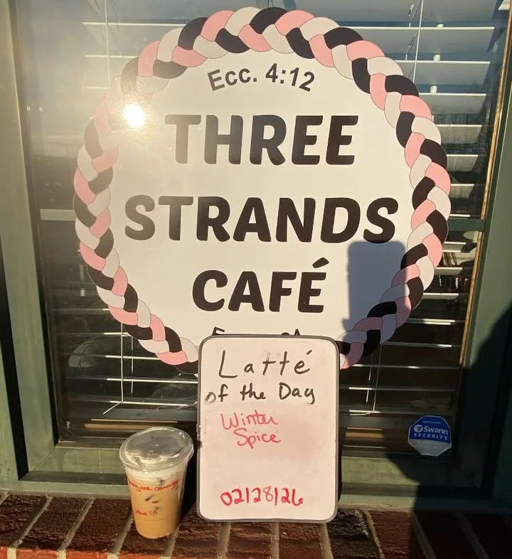 A café window featuring a sign for the 'Latte of the Day' called 'Winter Spice', alongside a cup of iced latte.