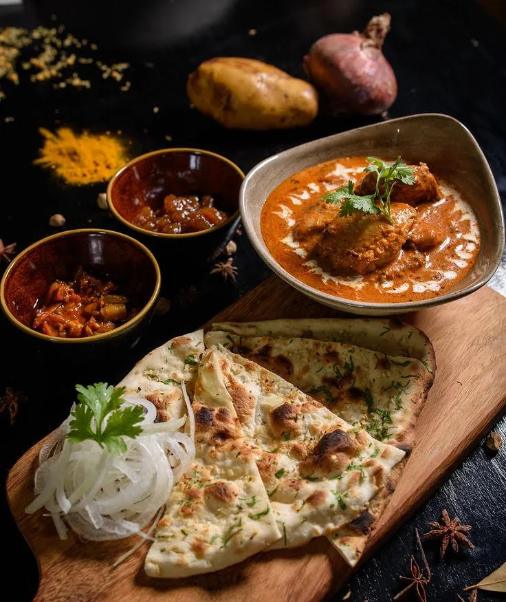 A colorful plate of savory snacks topped with yogurt, chutneys, and pomegranate seeds, garnished with fresh cilantro and served with side bowls of ingredients.