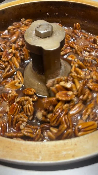 Pecans being mixed in a machine, showing a glossy coating as they rotate in a bowl.