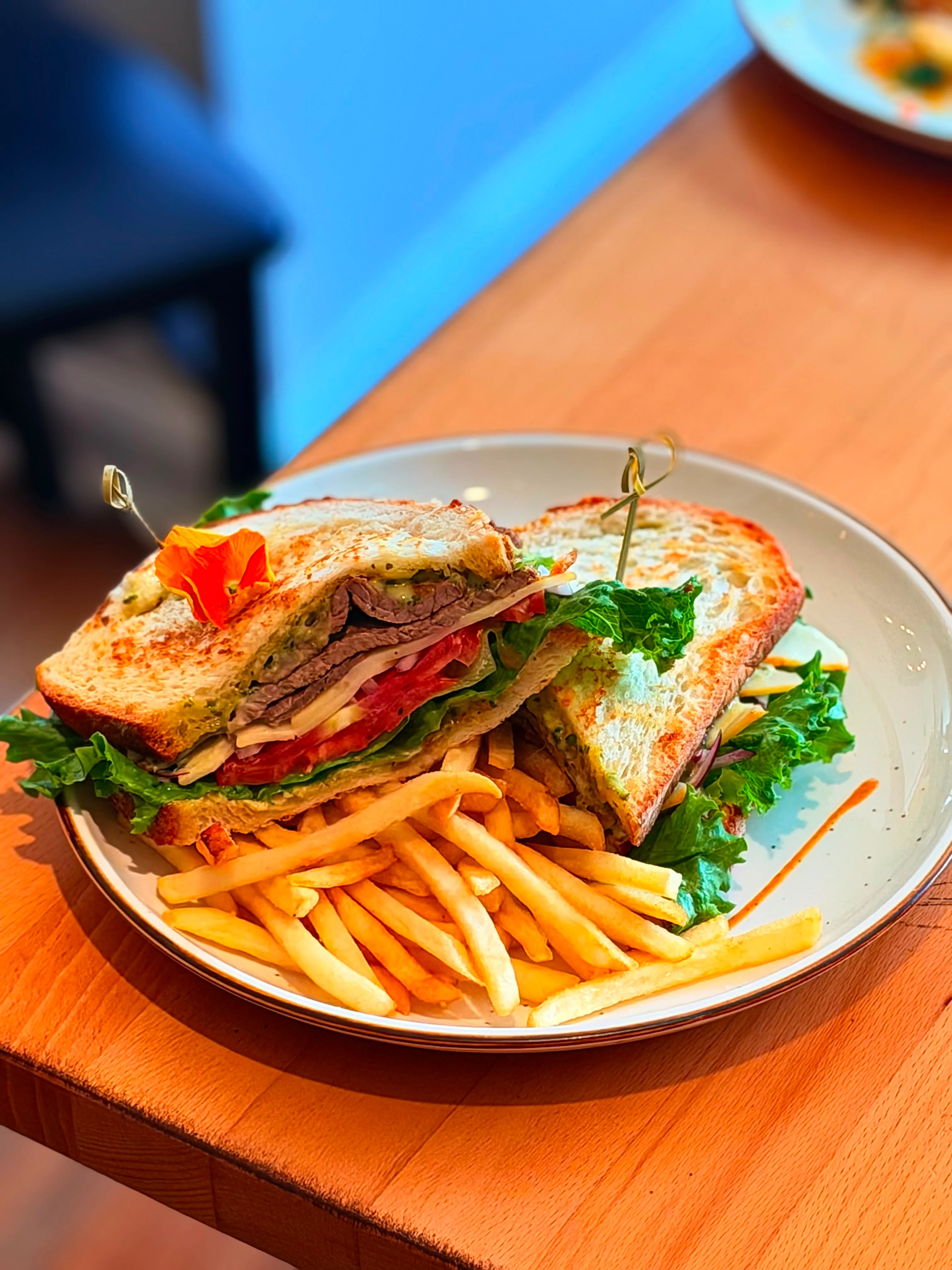 A hearty sandwich with layers of meat, lettuce, tomato, and other fresh ingredients, served with a side of golden fries.