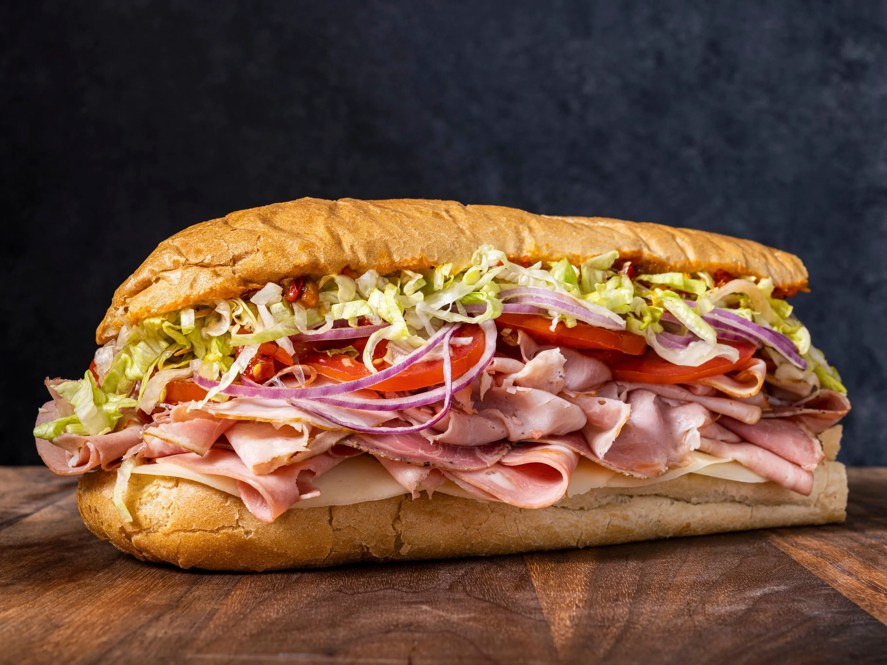 A large sub sandwich filled with meats, lettuce, tomatoes, and onions.