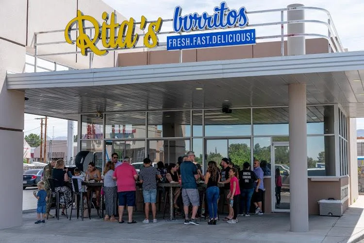 A busy outdoor area in front of a burrito restaurant, with a crowd of people enjoying their meals.
