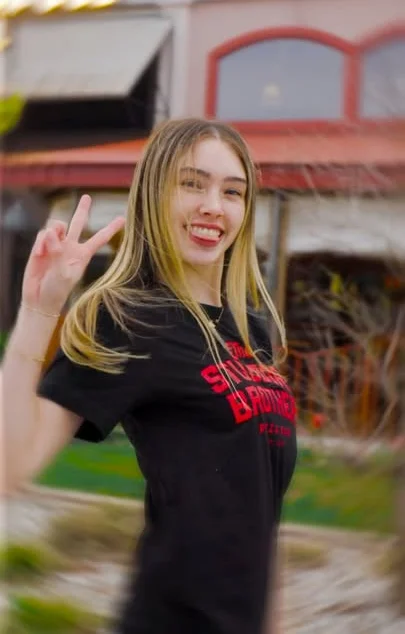 Smiling young woman posing outdoors with a peace sign