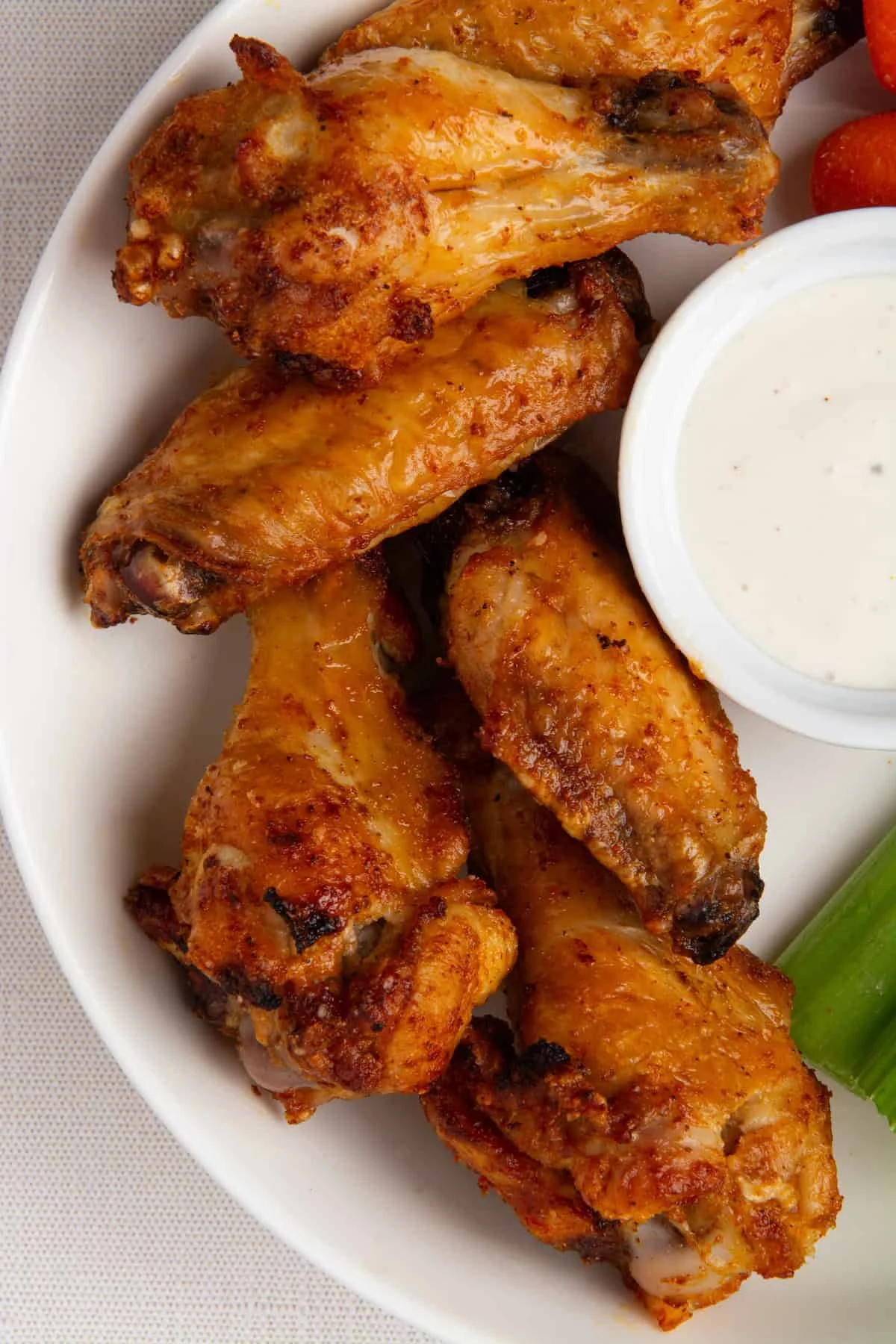 A plate of crispy chicken wings, golden brown and seasoned. Accompanied by a small bowl of creamy dipping sauce.