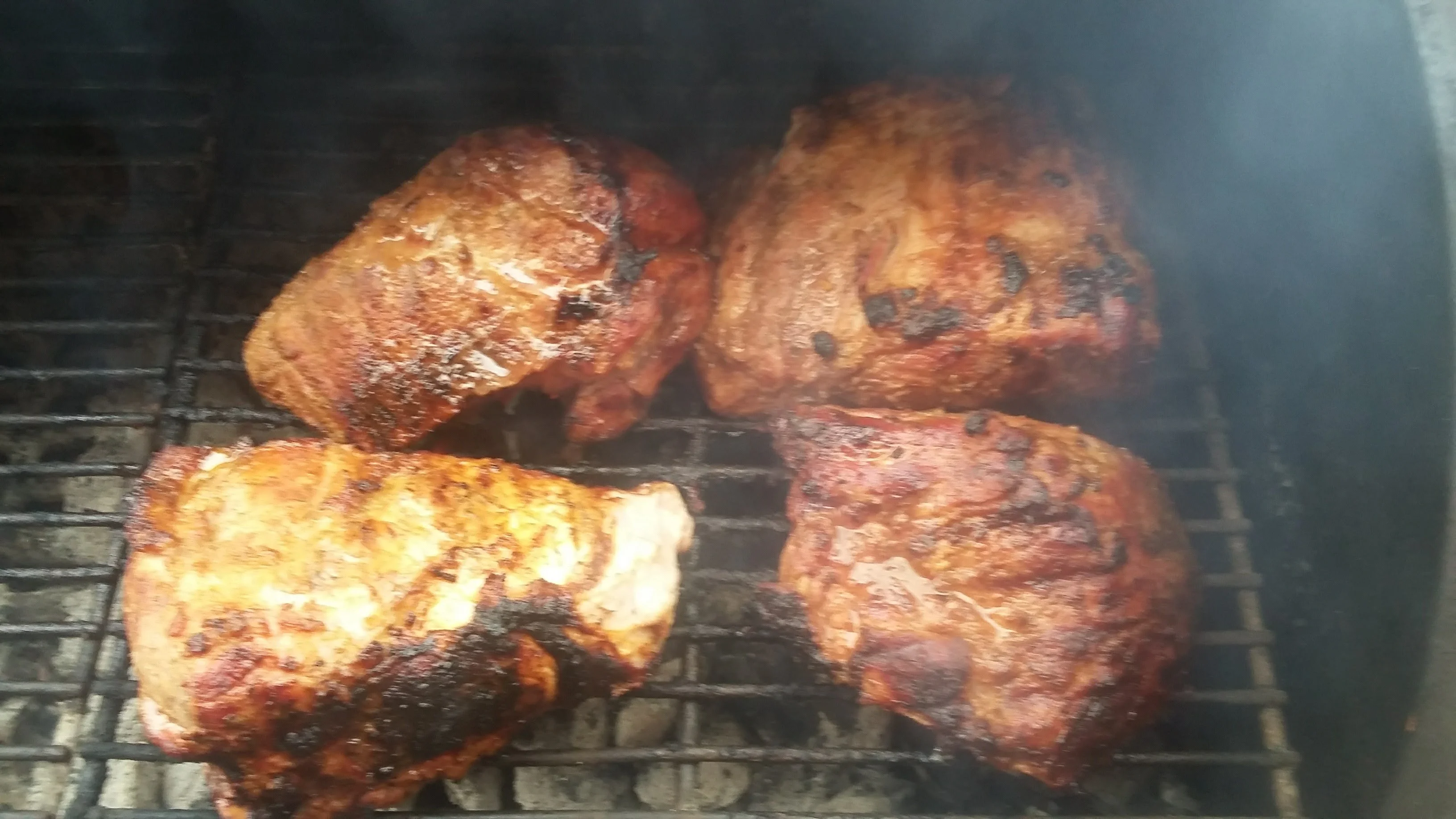 Several pieces of meat grilling over an open flame, displaying a charred and smoky appearance.