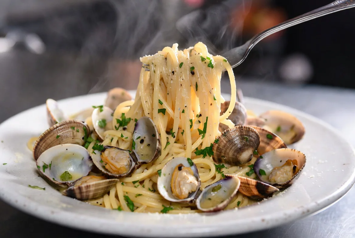 Plate of spaghetti with clams and parsley, steaming and garnished.