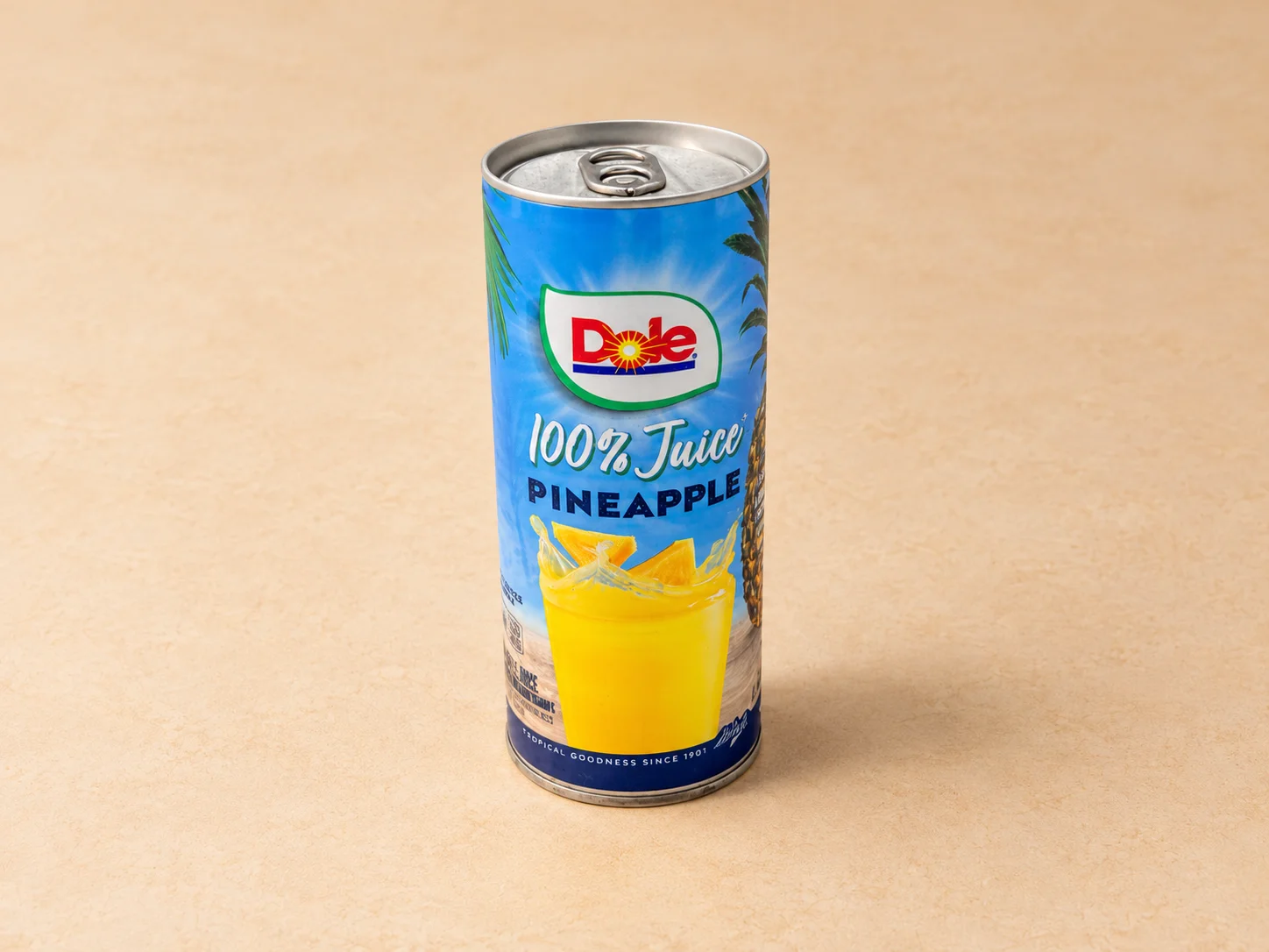 A can of pineapple juice stands upright on a surface. The can is brightly designed with images of pineapples and indicates that it contains 100% juice.