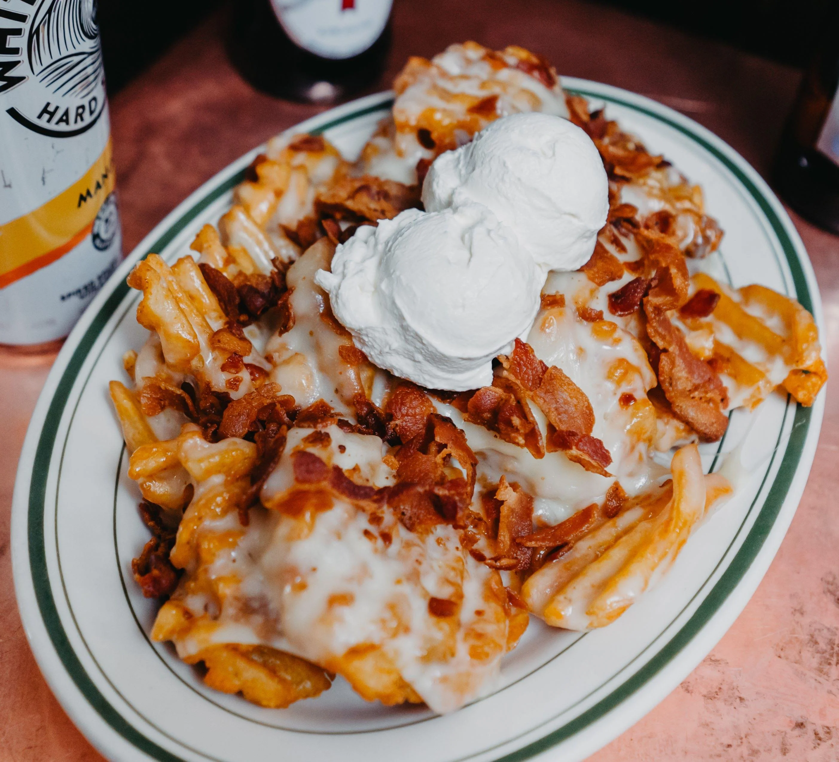 A plate of loaded fries topped with cheese, bacon bits, and two dollops of whipped cream. The fries are crunchy and appear indulgent.