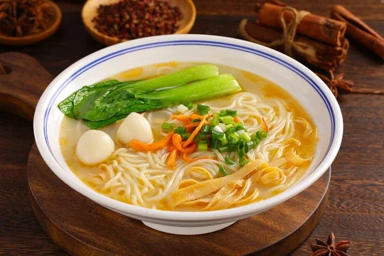 Bowl of Chinese noodle soup with greens and fish balls