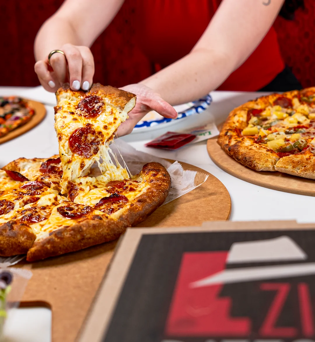 A hand reaching for a slice of pepperoni pizza with melted cheese.