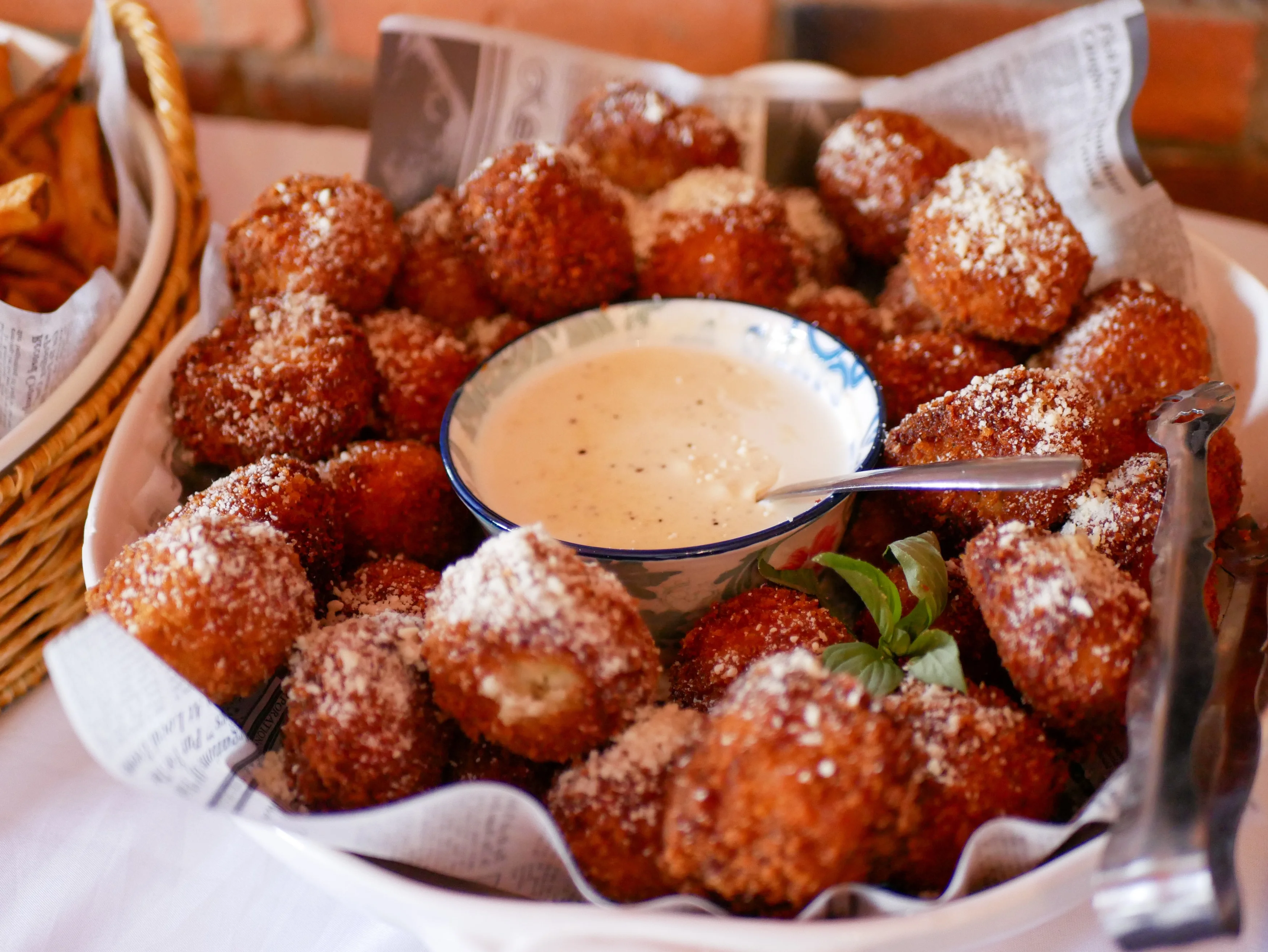 A large bowl filled with golden-brown fried snacks, dusted with cheese and served with a creamy dipping sauce.