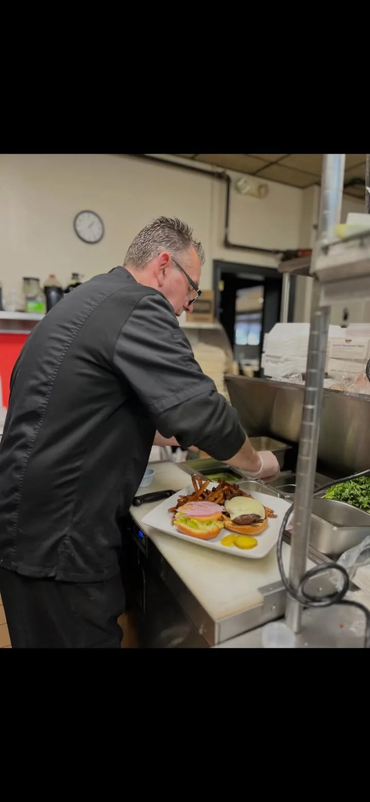 A chef at work in a kitchen, preparing a plate of burgers and fries. The chef is focused on arranging the food on the countertop.