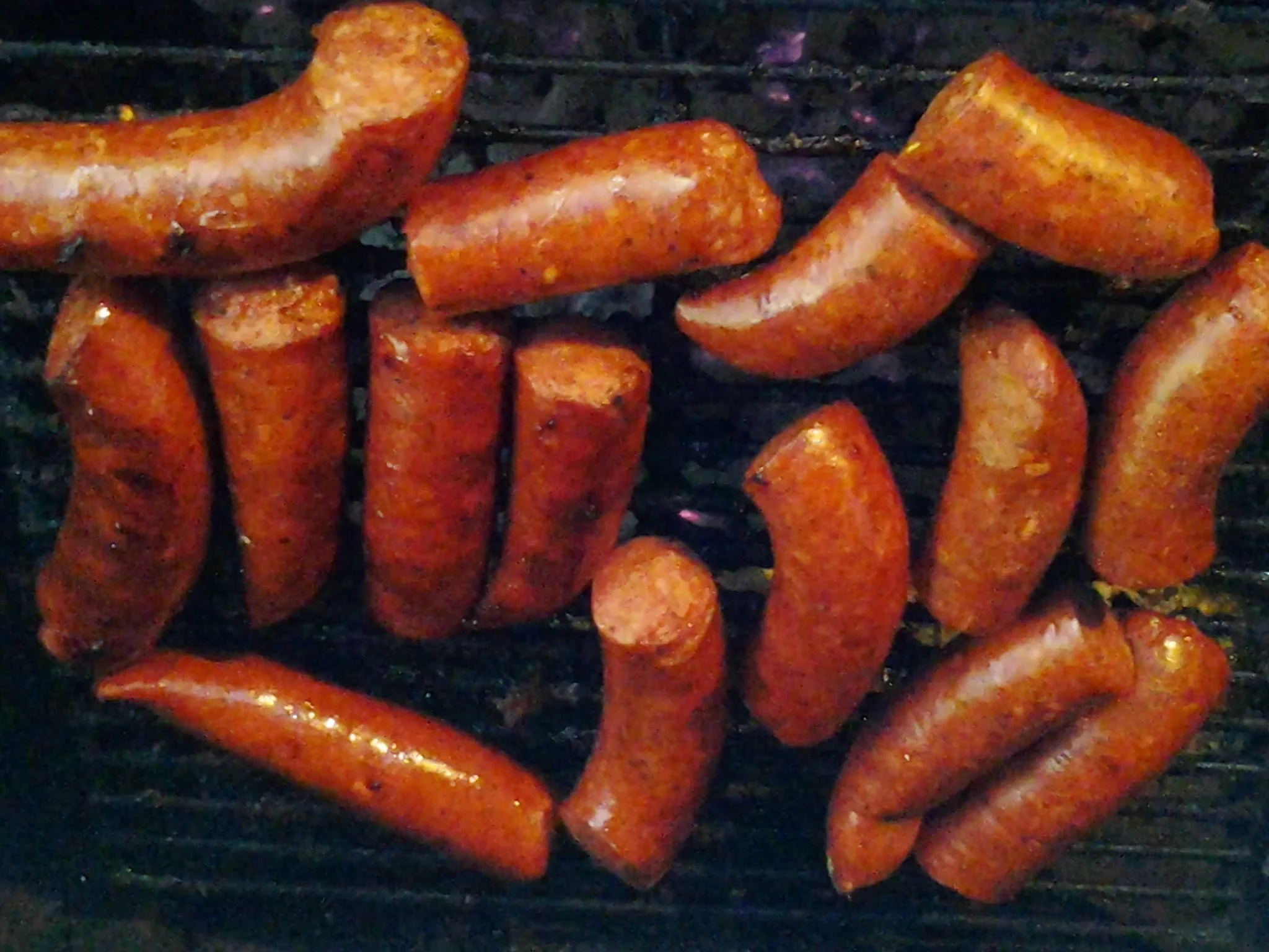 Grilled sausages arranged on a barbecue grill, showcasing a rich, brown color and textured surface.