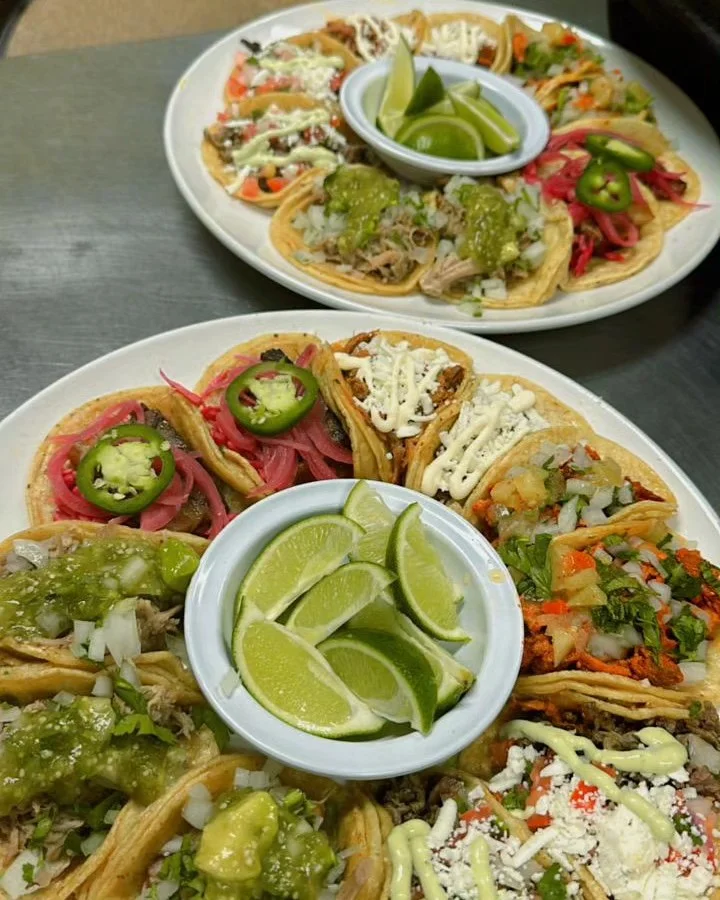 A delicious assortment of tacos arranged on a plate, topped with various ingredients and accompanied by lime wedges.