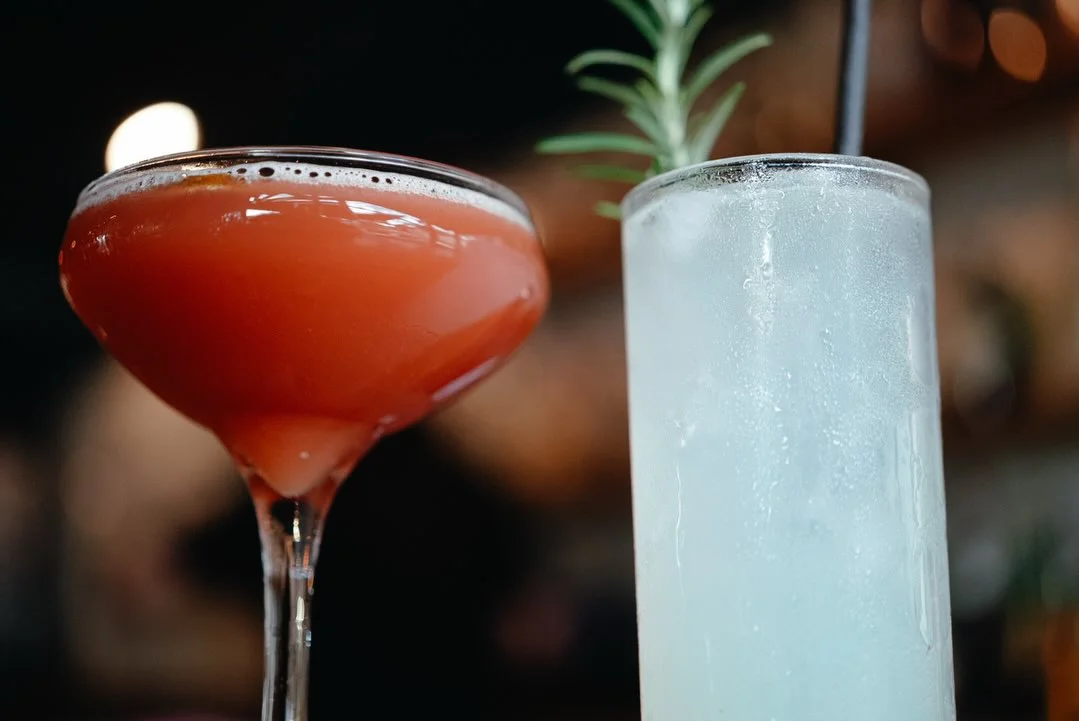 A close-up of a glass filled with a reddish beverage, set against a blurred background with food items.