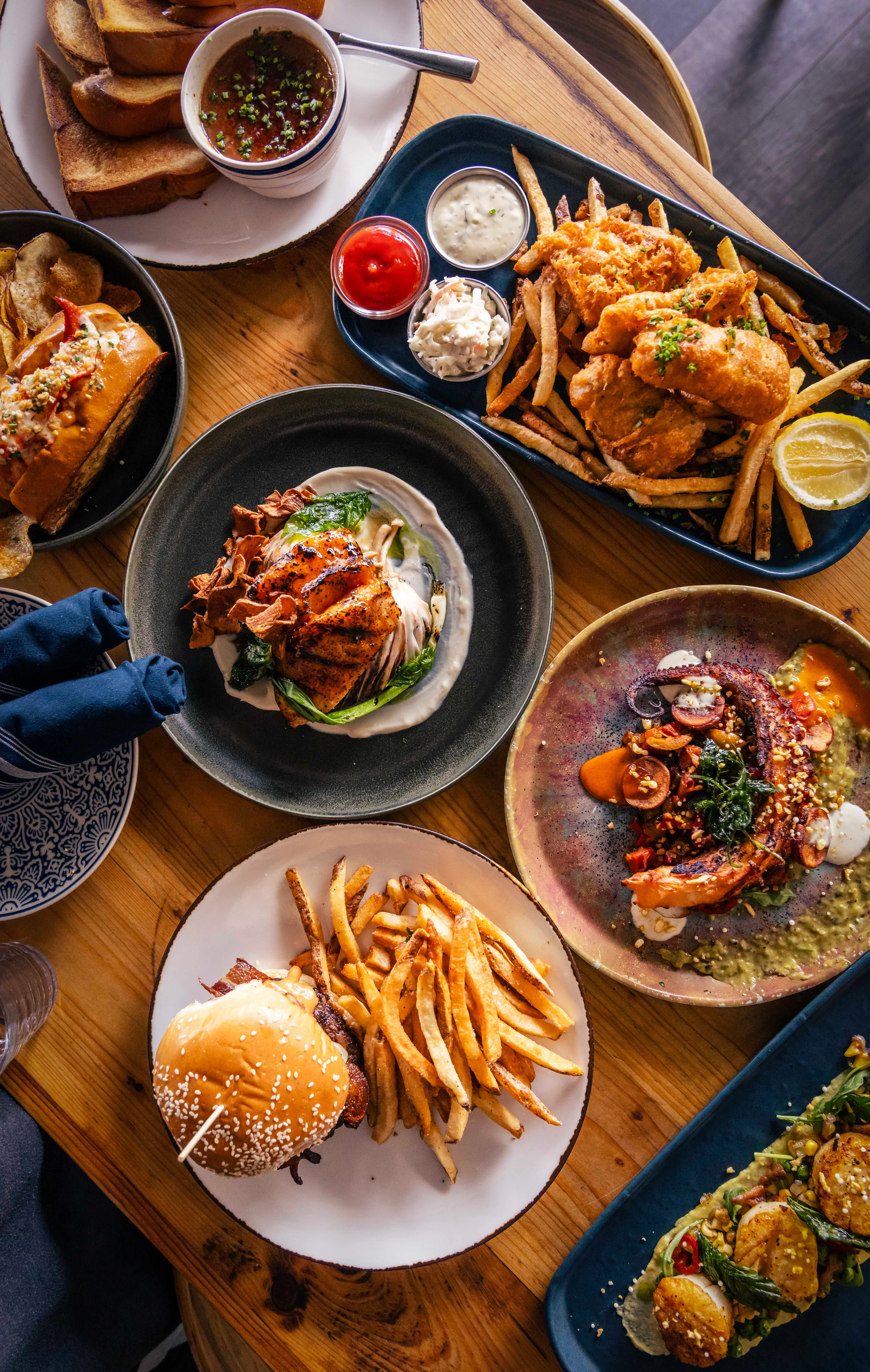 A plate of crispy fried shrimp arranged on a bed of fresh greens, including arugula and peas, with a charred lemon wedge.
