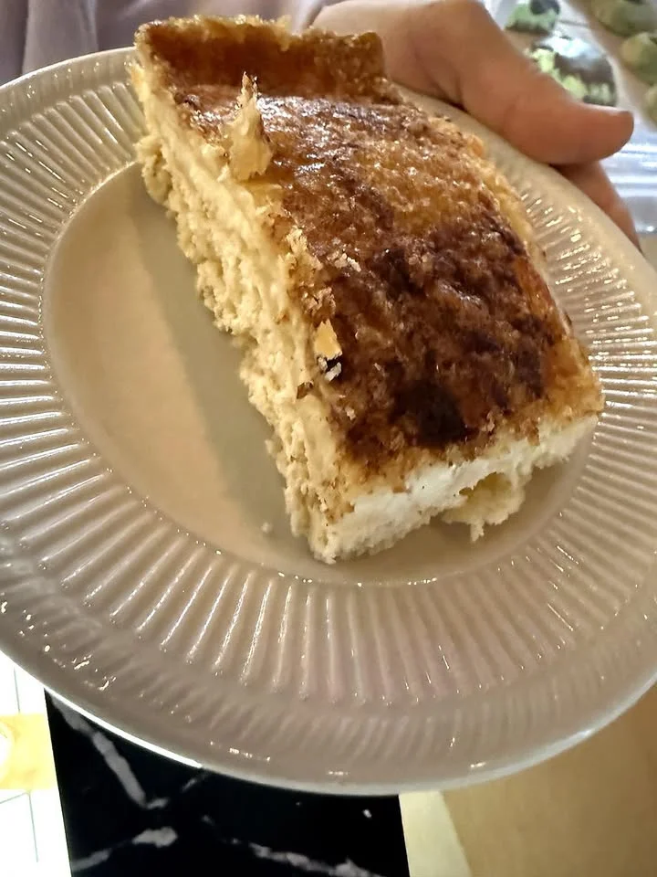 A slice of cake on a decorative plate, held by a person; the cake has a light, fluffy texture and a golden crust.
