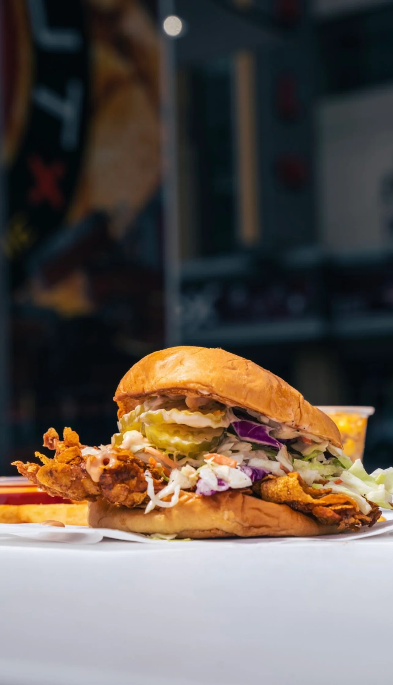 A piled sandwich featuring crispy fried chicken, lettuce, mayo, and pickles, served with a side of crispy fries.