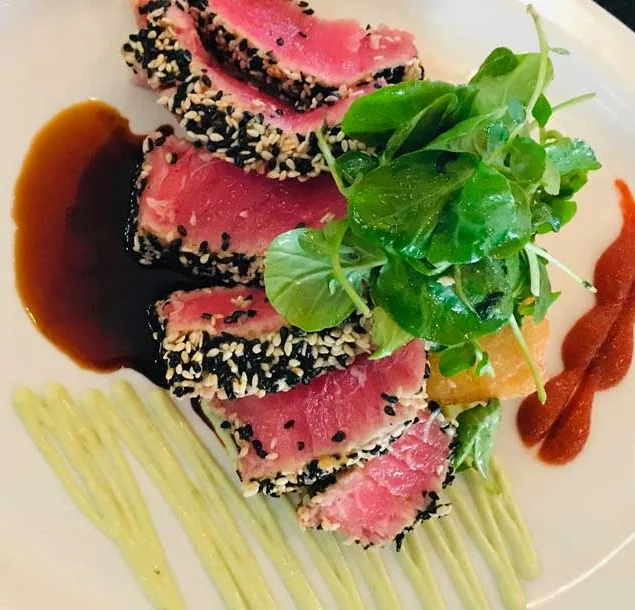 Large white plate with tuna tartare, some green leaves, and brown and green sauces smeared on the plate