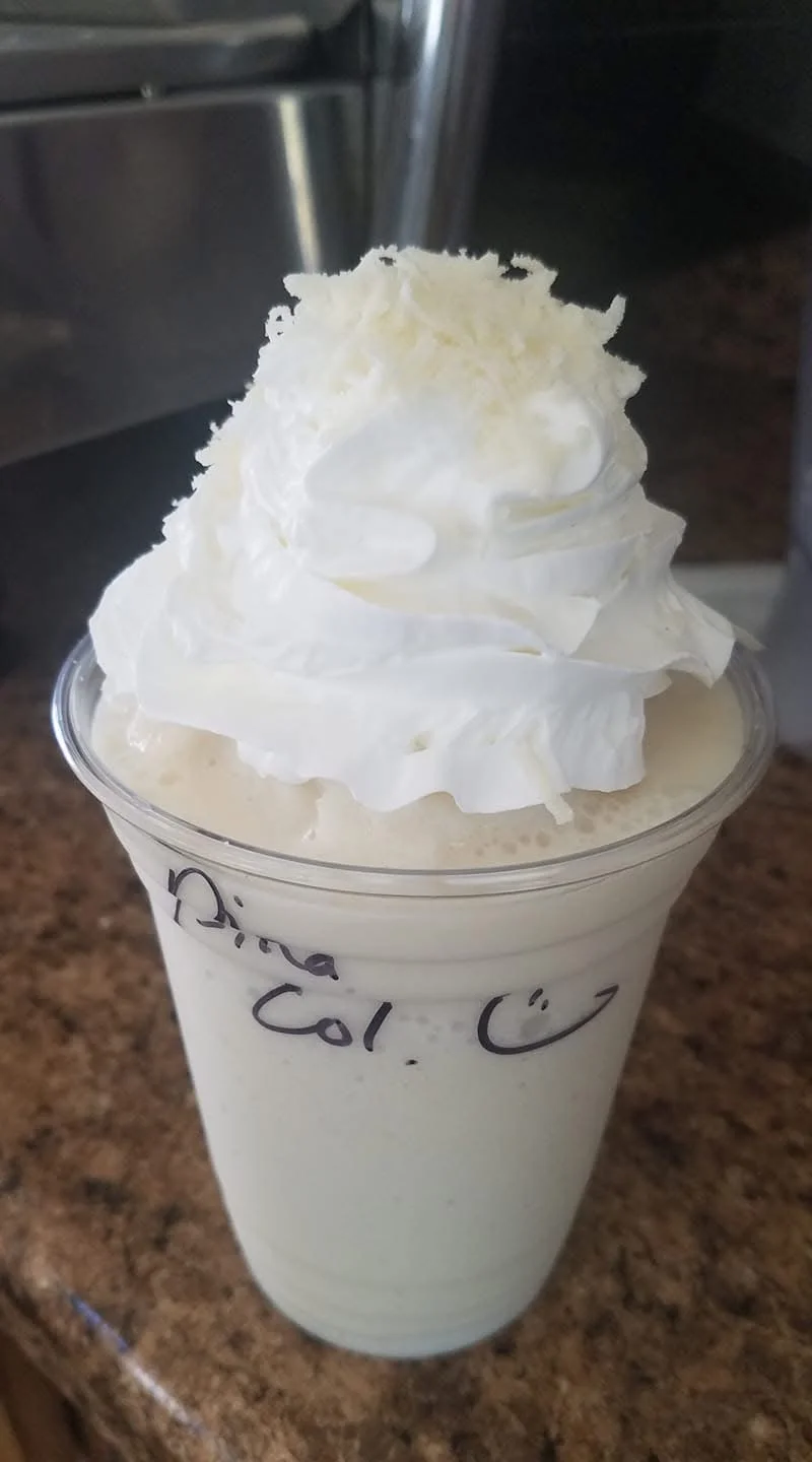 Two cups of creamy pumpkin spice drink topped with whipped cream and sprinkled with cinnamon. A small pumpkin and a cinnamon stick are nearby.