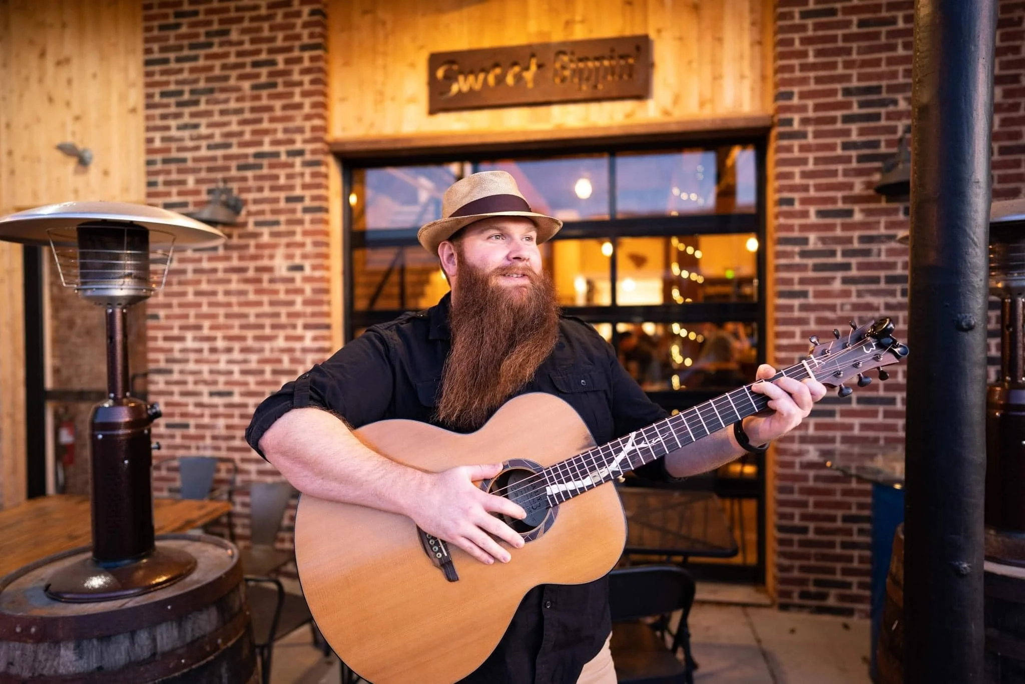 Musician performing outside a rustic restaurant with guitar