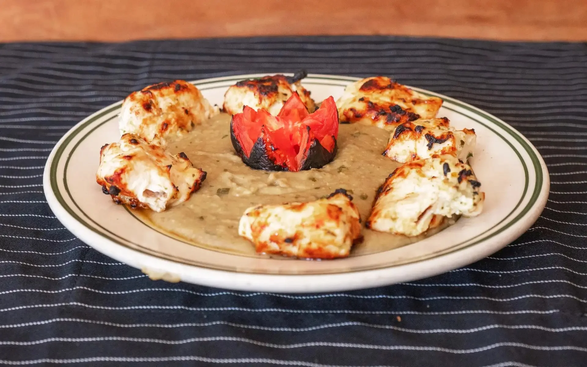 Grilled chicken served on a plate with a creamy sauce and garnished tomato.
