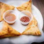 A plate of samosas served with two dipping sauces, one brown and one red.