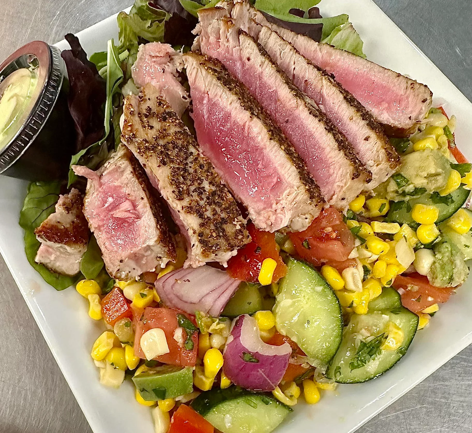 Sliced seared steak on a bed of fresh salad with vegetables and dressing.