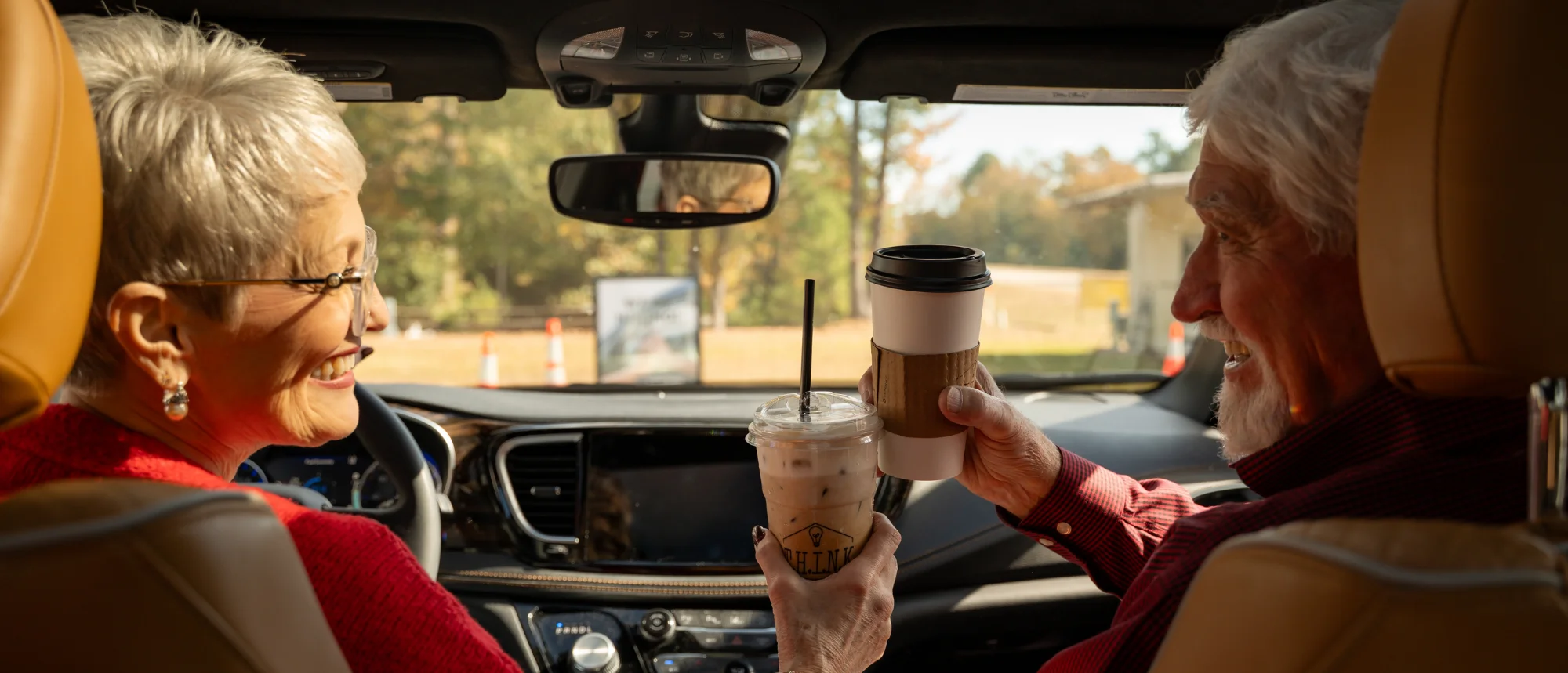 Man and woman celebrating with hot coffee and iced coffee in vehicle