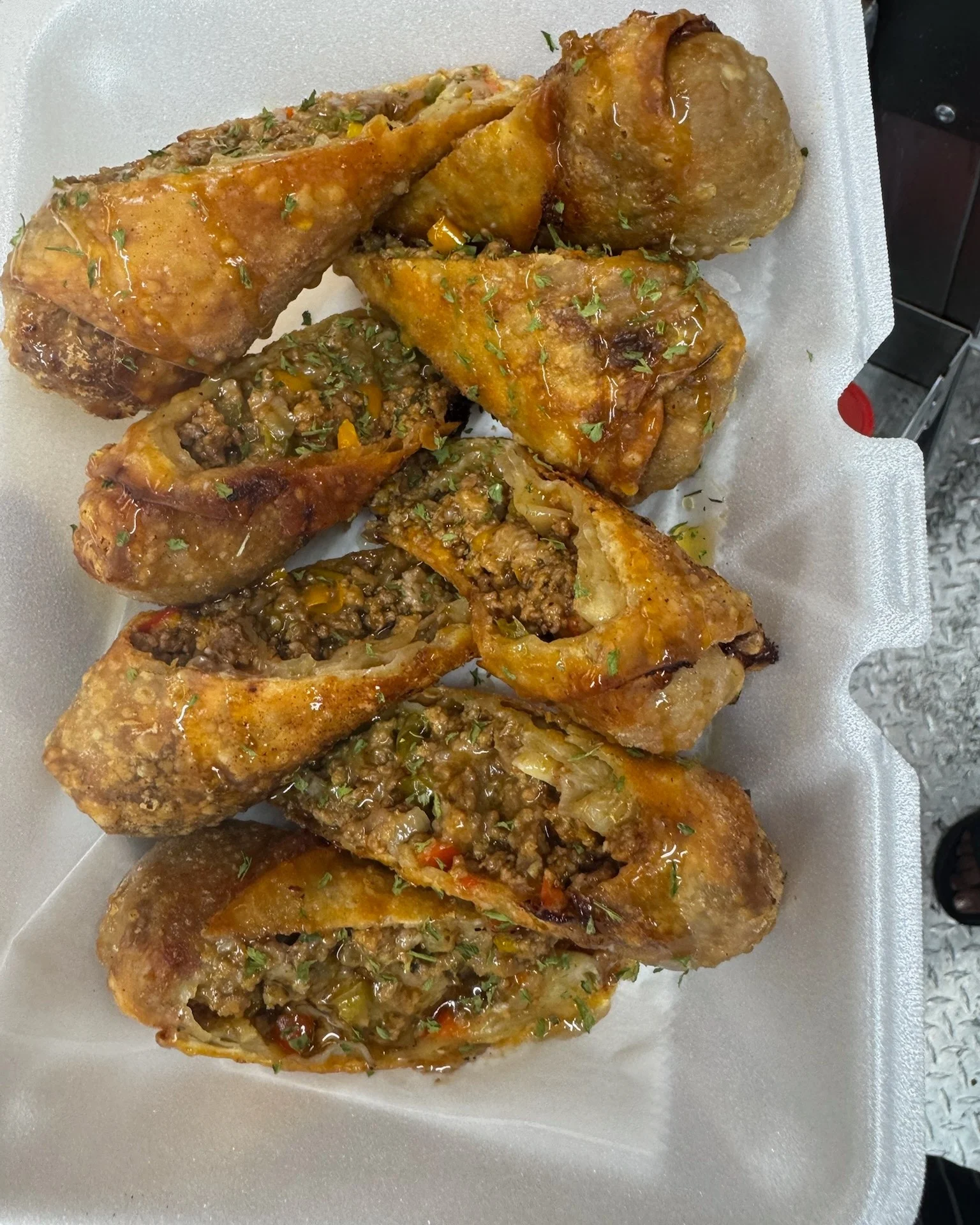 A hand holding a takeout container with four savory balls drizzled with a creamy sauce and topped with green herbs.
