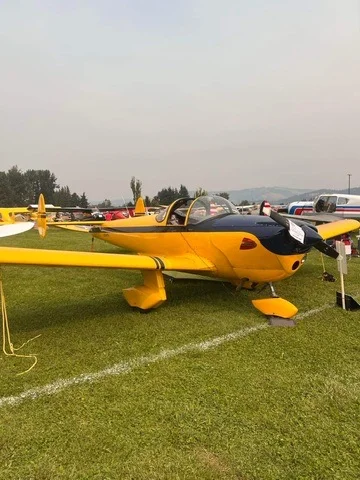 Yellow light aircraft parked on green grass at an airshow