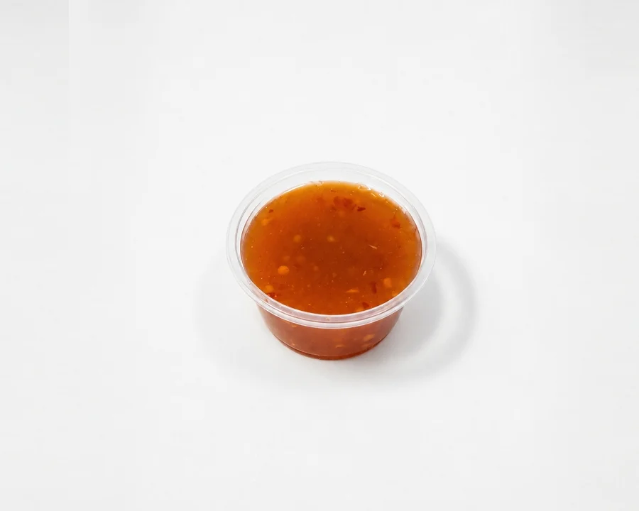 A small container of a reddish-brown sauce, appearing smooth and possibly spicy.