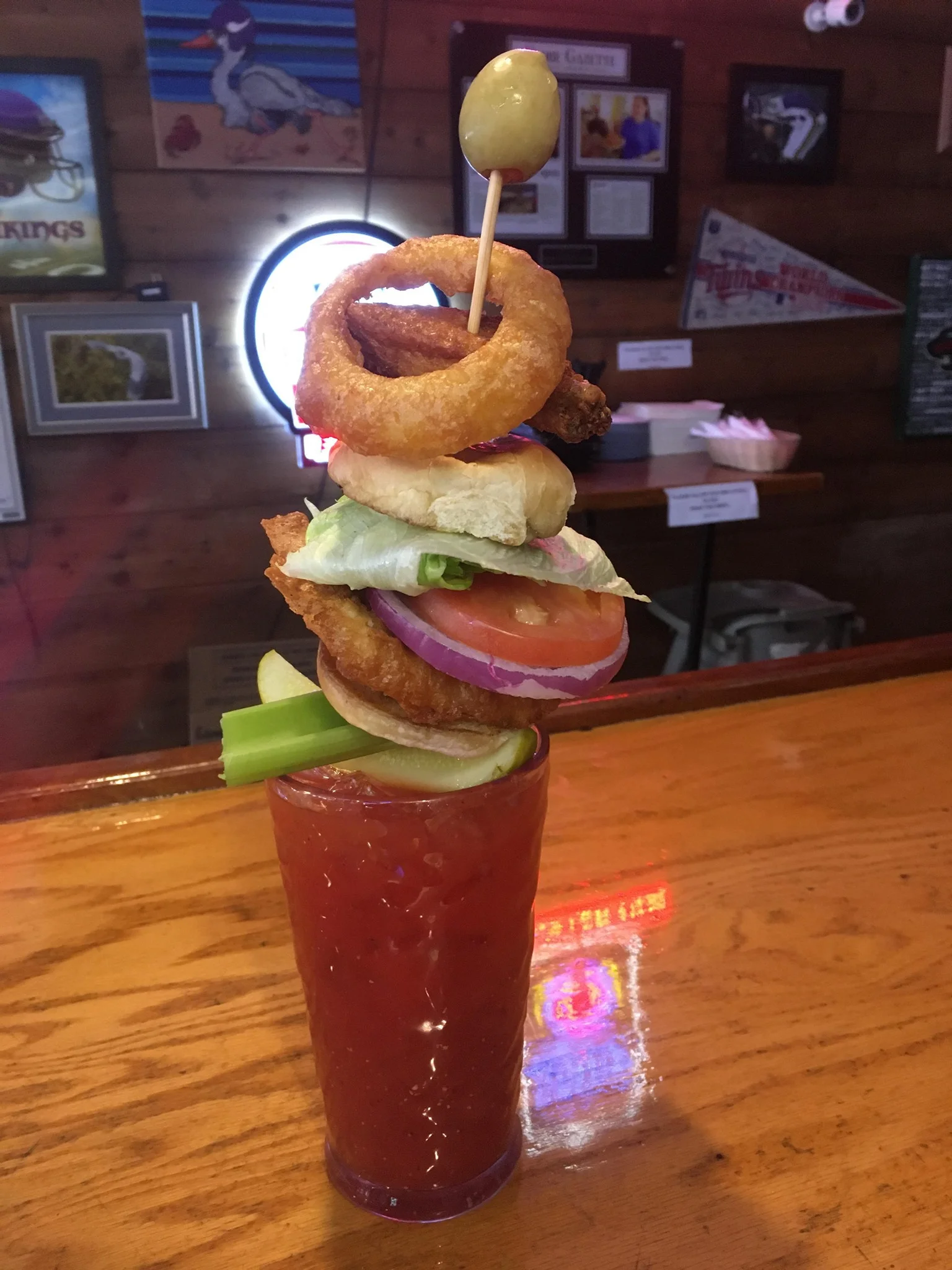 A tall Bloody Mary garnished with various food items on a wooden bar.